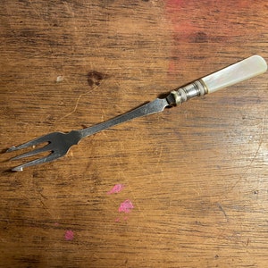 May include: A silver fork with a mother-of-pearl handle. The fork is on a wooden surface.
