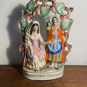 May include: A ceramic figurine of three women, two standing and one sitting, with a leafy archway above them. The figurine is painted in bright colors and has the words "FORTUNE TELLER" written on the base.
