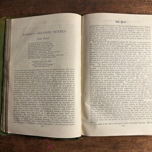 Pode incluir: Livro aberto com capa verde e p&aacute;ginas envelhecidas. O texto "ESSAYS - SECOND SERIES" e "THE POET" &eacute; vis&iacute;vel. O livro est&aacute; sobre uma superf&iacute;cie de madeira, mostrando o texto e sua apar&ecirc;ncia envelhecida.