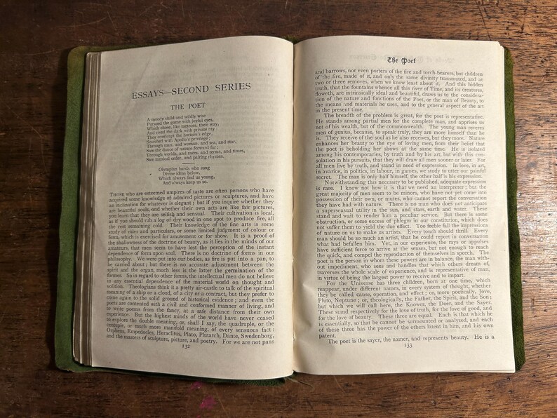 Pode incluir: Livro aberto com capa verde e p&aacute;ginas envelhecidas. O texto "ESSAYS - SECOND SERIES" e "THE POET" &eacute; vis&iacute;vel. O livro est&aacute; sobre uma superf&iacute;cie de madeira, mostrando o texto e sua apar&ecirc;ncia envelhecida.