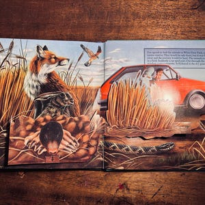 K&ouml;nnte beinhalten: Illustration eines offenen Buches mit einem Fuchs, einem Kaninchen und einem Vogel auf einem Feld. Rechts ist ein rotes Auto mit einer Person darin zu sehen. Der Text lautet: "Fox stimmte zu, die Tiere zum White Deer Park zu f&uuml;hren..." und "Pl&ouml;tzlich raste ein Auto vorbei."