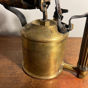 Pode incluir: Um ma&ccedil;arico vintage de lat&atilde;o com cabo preto e bico de lat&atilde;o. O ma&ccedil;arico tem um r&oacute;tulo que diz "S.L.Sivert Patent" e "Estocolmo".