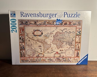Può includere: Un puzzle Ravensburger da 2000 pezzi con un design a mappa del mondo vintage. La scatola mostra una mappa dettagliata in stile antico con illustrazioni e testo intricati. La scatola ha il logo Ravensburger e le parole "Premium Puzzle Softclick Technology".