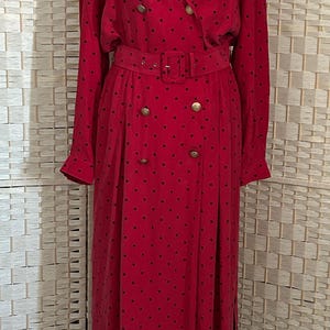 May include: A red vintage dress with a double-breasted design and a matching belt. The dress features small black polka dots and gold-colored buttons. The long-sleeved dress is displayed on a mannequin.