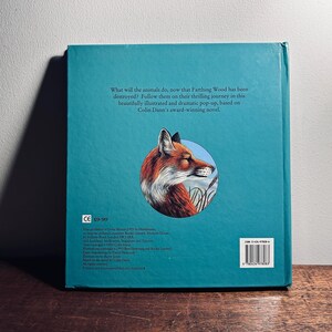 K&ouml;nnte beinhalten: Ein t&uuml;rkisfarbenes Buch mit einer Illustration eines Fuchses auf dem hinteren Einband. Der Fuchs ist in einem kreisf&ouml;rmigen Rahmen dargestellt. Der Text auf der R&uuml;ckseite lautet: "Was werden die Tiere tun, nachdem Farthing Wood zerst&ouml;rt wurde?"