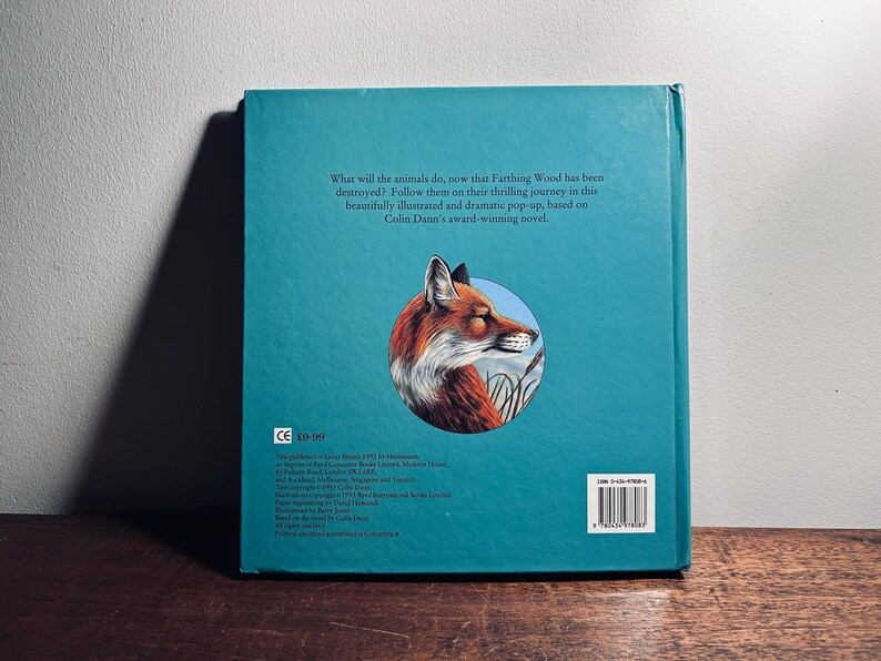 K&ouml;nnte beinhalten: Ein t&uuml;rkisfarbenes Buch mit einer Illustration eines Fuchses auf dem hinteren Einband. Der Fuchs ist in einem kreisf&ouml;rmigen Rahmen dargestellt. Der Text auf der R&uuml;ckseite lautet: "Was werden die Tiere tun, nachdem Farthing Wood zerst&ouml;rt wurde?"