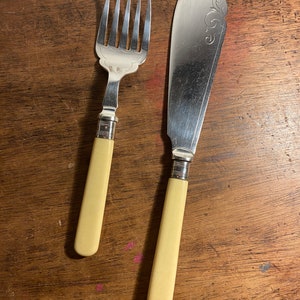 Könnte beinhalten: Ein Besteckset aus Silber mit Elfenbeinstielen. Gabel und Messer haben verzierte Designs auf dem Metall.
