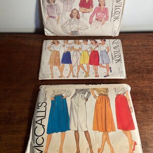 May include: Three vintage sewing patterns for skirts. The top pattern is for a blouse and skirt, the middle pattern is for a skirt, and the bottom pattern is for four different skirts. The patterns are all from the 1970s and feature illustrations of women wearing the garments.