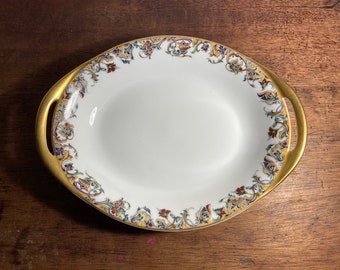 May include: An oval serving dish with gold handles and a white background. The rim is decorated with a floral pattern in shades of blue, green, red, and yellow.