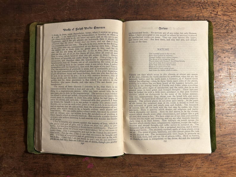 Pode incluir: Livro aberto com capa verde, exibindo texto de "Works of Ralph Waldo Emerson" e "Nature". As p&aacute;ginas est&atilde;o envelhecidas, com texto vis&iacute;vel. O livro est&aacute; aberto sobre uma superf&iacute;cie de madeira.