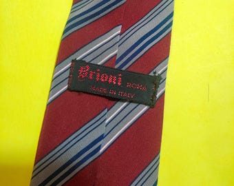 May include: A burgundy tie with blue and gray diagonal stripes. The tie has a label that reads "Brioni ROMA MADE IN ITALY". The tie is made of a smooth fabric and is suitable for formal occasions.