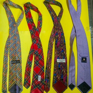 May include: Four neckties in various patterns and colors are displayed against a yellow background. The ties include a blue and gold striped tie, a red plaid tie, a paisley tie, and a purple dotted tie. Each tie has a label.