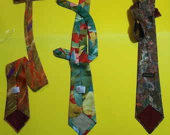 Può includere: Tre cravatte di seta colorate su sfondo giallo. Una cravatta presenta un motivo floreale con tonalità verdi, rosse e gialle. Un'altra cravatta ha un design astratto marrone e arancione. La terza cravatta ha un motivo geometrico con la parola "Zodiac".