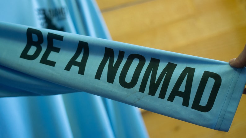 May include: A light blue long-sleeved shirt with the text "BE A NOMAD" printed in black.