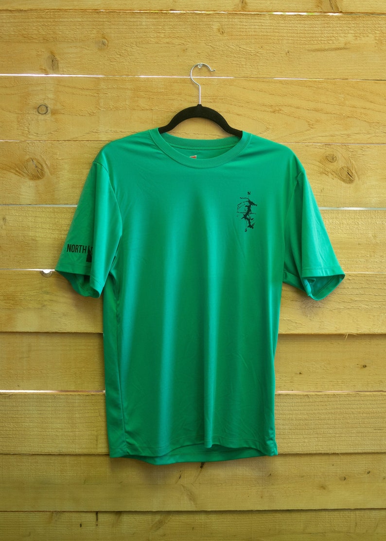 May include: A green short-sleeved t-shirt with a black compass design on the front and "NORTH" printed on the left sleeve.