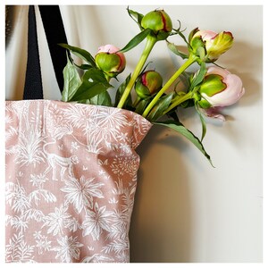 Puede incluir: Una bolsa de tela rosa y blanca con estampado tropical de monos y palmeras. La bolsa est&aacute; llena de un ramo de peon&iacute;as rosas y verdes.