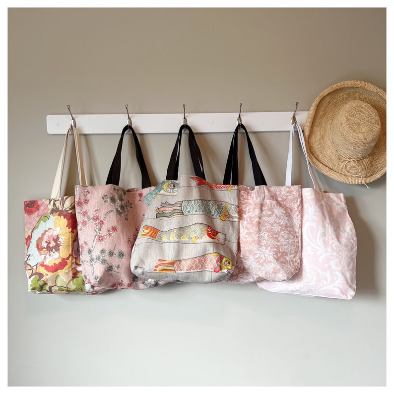 Puede incluir: Cinco bolsas de tela colgadas de ganchos. Las bolsas est&aacute;n hechas de diferentes telas y tienen varios patrones. Una bolsa tiene un patr&oacute;n floral, otra tiene un patr&oacute;n floral rosa y blanco, otra tiene un patr&oacute;n de peces, otra tiene un patr&oacute;n floral rosa y blanco y la &uacute;ltima bolsa tiene un patr&oacute;n floral rosa y blanco.