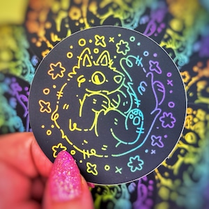 Puede incluir: Una pegatina negra y blanca con un contorno de arcoíris de un lobo de dibujos animados con una huella de pata en su pie. El lobo está rodeado de estrellas y el texto "the" está escrito debajo.