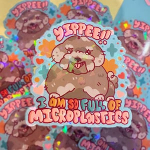 May include: A holographic sticker featuring a cartoon dog with the text "YIPPEE!! I AM SO FULL OF MICROPLASTICS". The dog is brown and white and has a pink tongue sticking out. The sticker is on a blue background with pink hearts and stars.