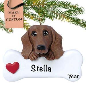 May include: A brown dachshund dog ornament with a white bone-shaped plaque. The plaque has a red heart and the text "Stella Year".