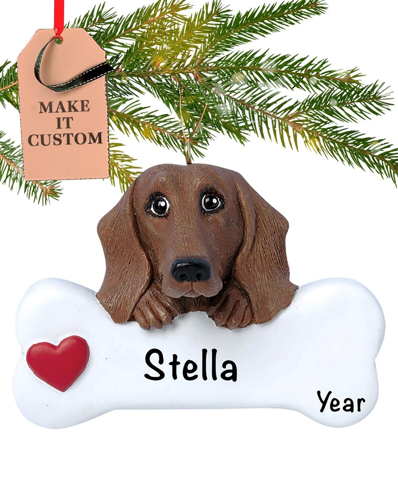 May include: A brown dachshund dog ornament with a white bone-shaped plaque. The plaque has a red heart and the text "Stella Year".