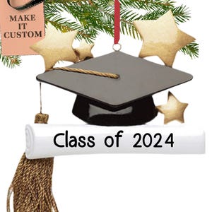 May include: Black graduation cap ornament with a gold tassel and a white scroll that says "Class of 2024". The ornament is decorated with gold stars.