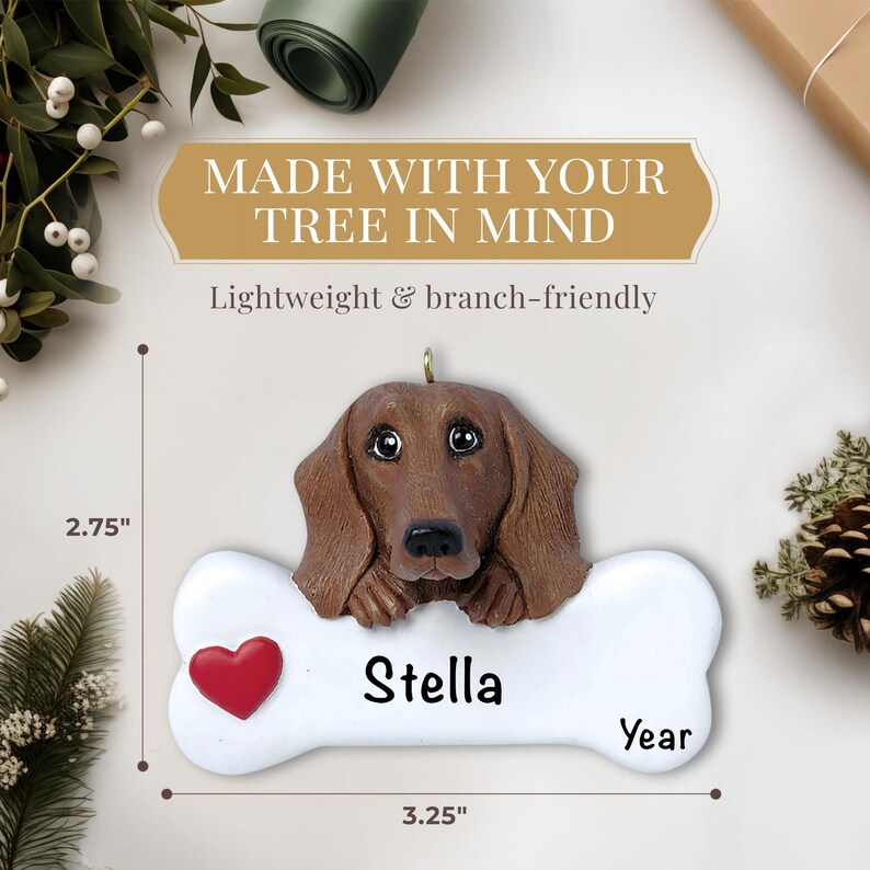 May include: A personalized Christmas ornament featuring a brown dachshund dog with a red heart and the name "Stella" on a white bone-shaped plaque. The ornament is 2.75 inches tall and 3.25 inches wide.