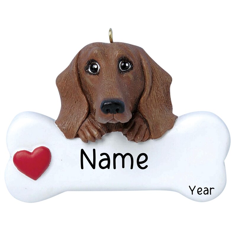 May include: A brown dachshund dog ornament with a bone-shaped plaque. The plaque has a red heart and the words "Name" and "Year".