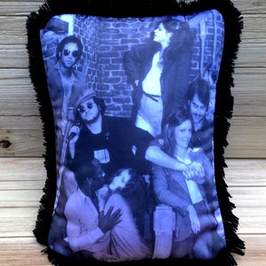 May include: A black and white photo of a group of people, printed on a throw pillow with black fringe. The pillow features a group of people in a brick alleyway.