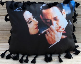 May include: Black throw pillow with a fringe border featuring a photo of a couple embracing. The couple is dressed in black and white clothing. The photo is in color.