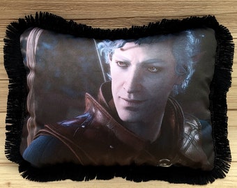 Puede incluir: Una almohada decorativa con un borde de flecos negros presenta una imagen de primer plano de un hombre con cabello azul que lleva una chaqueta de cuero marrón. El hombre mira directamente al espectador con una leve sonrisa.