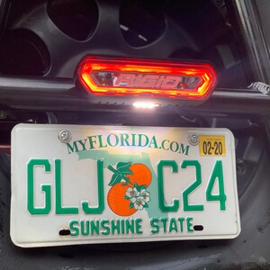 May include: A white Florida license plate with green lettering that reads "GLJ C24" and the text "MYFLORIDA.COM" and "SUNSHINE STATE". A red and white light bar is mounted above the license plate.