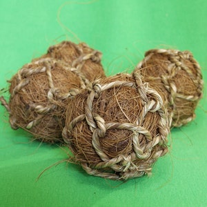 May include: Three brown, woven coconut husk balls on a green background. The balls are made of natural fibers and have a rough texture.