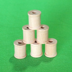 May include: A stack of six wooden spools arranged in a pyramid shape on a green surface.