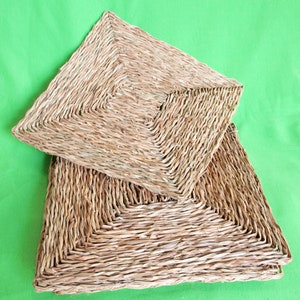 May include: Two square woven mats made of natural fibers, stacked on top of each other. The mats are a light brown color and have a woven pattern.