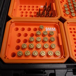 May include: A black storage case with orange compartments filled with ammunition. One compartment is labelled "9MM". Various bullets are visible, including .22 calibre and 9mm rounds, neatly arranged in rows.