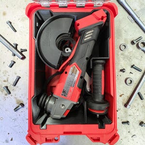 May include: A red and black power tool set, including a grinder, stored in a red case. The grinder has a black blade guard and a black and red handle. Various tools and screws are scattered around the case.