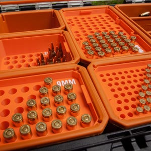 May include: An open black and orange storage case with multiple compartments filled with ammunition. The ammunition is arranged in neat rows and includes various bullet types. The case is designed for organisation and transport.