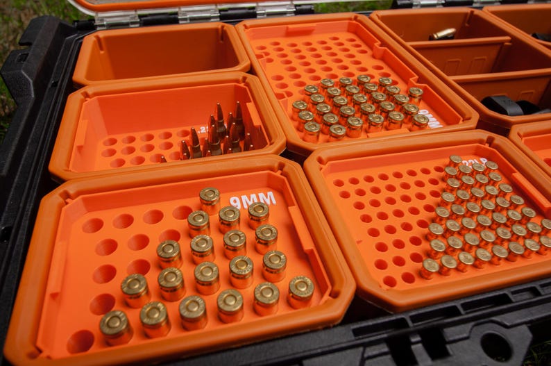 May include: An open black and orange storage case with multiple compartments filled with ammunition. The ammunition is arranged in neat rows and includes various bullet types. The case is designed for organisation and transport.