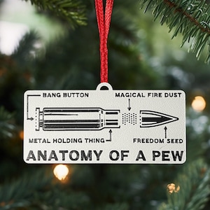 May include: A rectangular, off-white Christmas ornament with a diagram of a bullet and the words "Anatomy of a Pew." The diagram includes labels like "Bang Button" and "Freedom Seed." A red ribbon is attached for hanging.