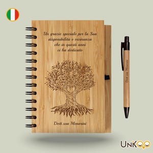 Könnte beinhalten: Ein Notizbuch- und Stift-Set aus Holz. Das Notizbuch hat eine Spiralbindung und ein lasergraviertes Baumdesign mit dem Text "Un grazie speciale per la Sua disponibilità e vicinanza che in questi anni ci ha dedicato" und "Dott.ssa Menarini". Der Stift hat den gleichen Text.