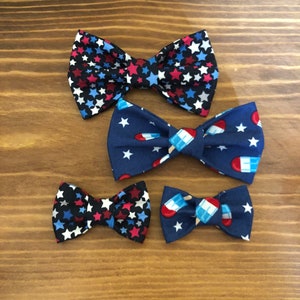 May include: Four bow ties in different patterns. Two are blue with white stars and red popsicle designs. One is blue with white stars and red stars. One is black with white stars and red stars.