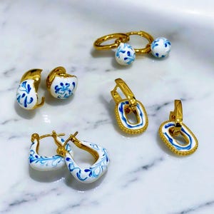 May include: A set of five pairs of gold earrings with blue and white porcelain designs. The earrings are in different shapes, including hoops, ovals, and circles.