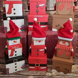 May include: A set of four stackable Christmas gift boxes featuring festive designs. The boxes are decorated with a snowman, Santa Claus, and a reindeer. Each box has a personalised name on the front: Callum, Jackson, Christina, and Kayla.