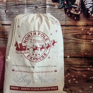 May include: A white canvas Santa sack with a red and white North Pole Express design. The sack has a drawstring closure and is decorated with snowflakes and stars. The text "checked once by Head Elf checked twice by Santa" is printed on the sack. The text "please deliver enclosed presents to: Any Name FROM: SANTA CLAUS, NORTH POLE" is also printed on the sack.