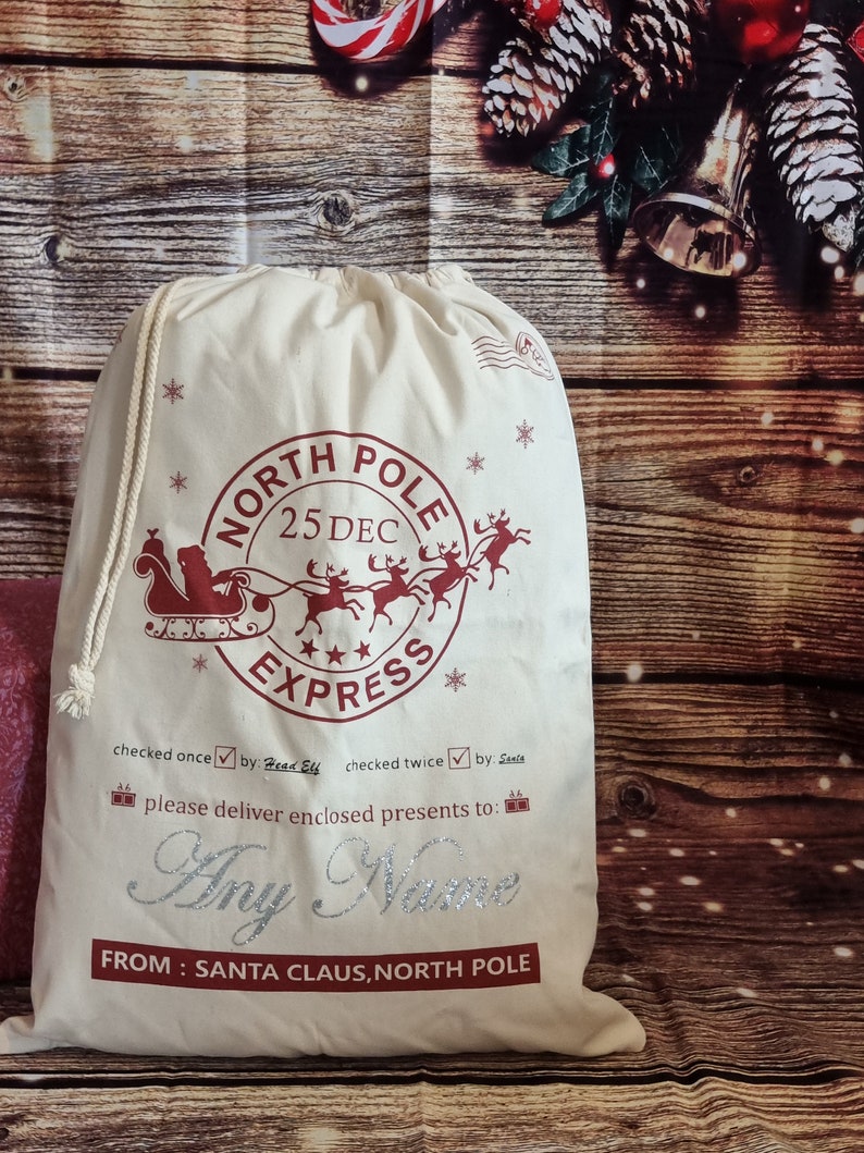 May include: A white canvas Santa sack with a red and white North Pole Express design. The sack has a drawstring closure and is decorated with snowflakes and stars. The text "checked once by Head Elf checked twice by Santa" is printed on the sack. The text "please deliver enclosed presents to: Any Name FROM: SANTA CLAUS, NORTH POLE" is also printed on the sack.