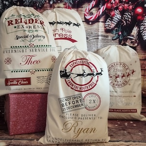 May include: Three white canvas Santa sacks with red and green designs. The sacks are decorated with reindeer, sleighs, and the words "Express Delivery", "North Pole Express", and "Do Not Open Before 25 December". The sacks are personalized with the names "Theo", "Ryan", and "My Name".