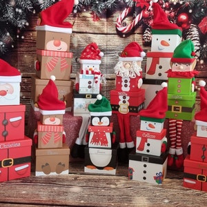 May include: A collection of Christmas gift boxes stacked on top of each other. The boxes are decorated with various festive themes, including penguins, reindeer, and Father Christmas. The boxes are all wrapped in red and white paper and have festive ribbons.
