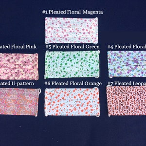 May include: Seven pleated face masks with various floral and patterned designs are displayed on a dark blue surface. The masks include floral patterns in magenta, pink, green, purple, and orange, along with a U-pattern and leopard print.