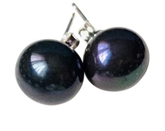 Puede incluir: Un par de pendientes de perlas negras. Las perlas redondas y brillantes tienen un brillo oscuro e iridiscente, que refleja toques de azul y verde. Los pendientes están engarzados en postes de plata.